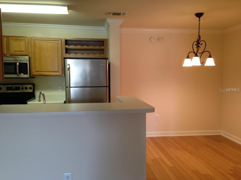A kitchen with stainless steel appliances and wood cabinets overlooks a dining area with hardwood floors — 18147 STERLING GATE CIRCLE UNIT 18147, TAMPA, FL