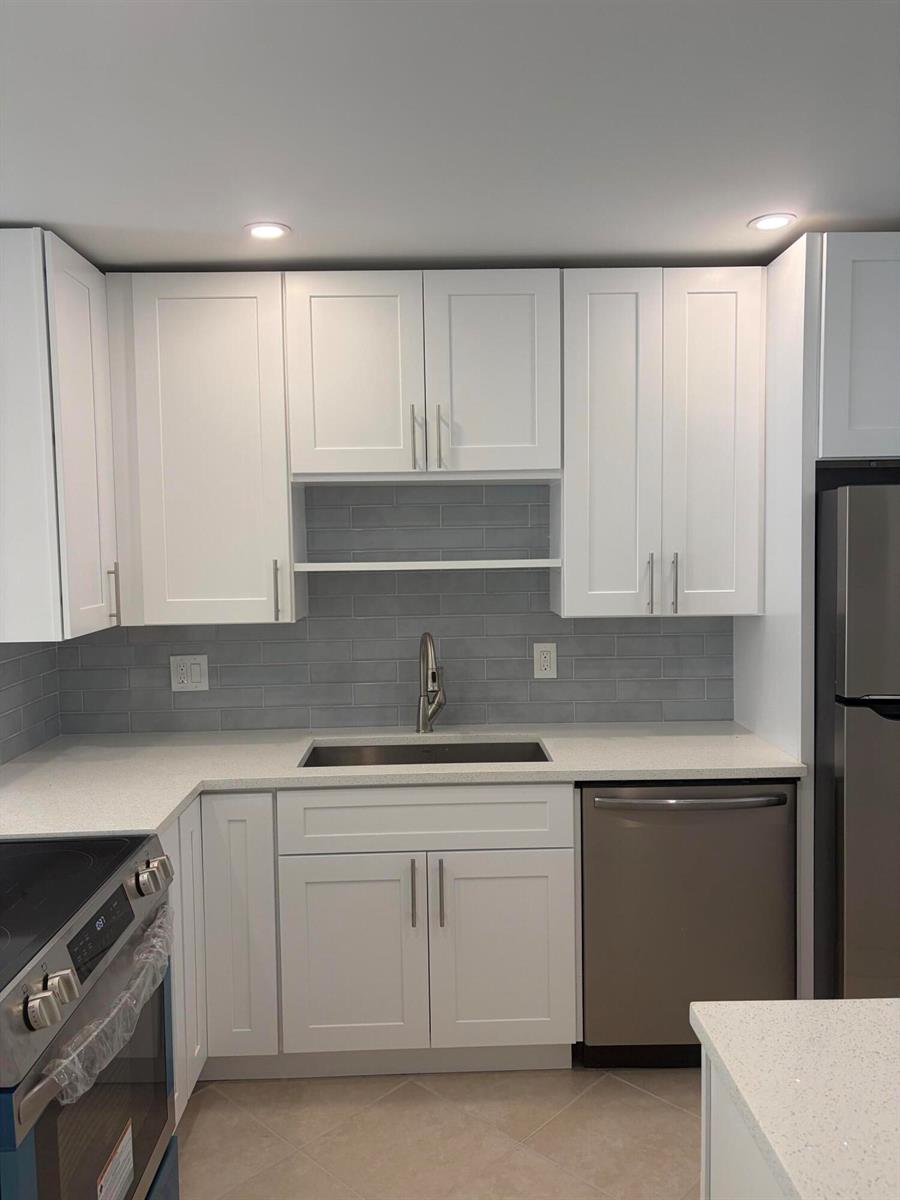 A kitchen features white shaker cabinets, gray subway tile backsplash, stainless steel appliances, and countertops — 2900 Fiore Way # 2110, Delray Beach FL 33445, DELRAY BEACH, FL