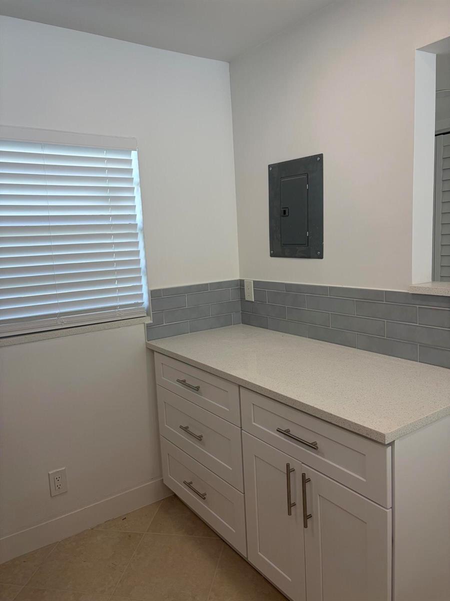A laundry room features white cabinets, a quartz countertop, gray subway tile, and an electrical panel — 2900 Fiore Way # 2110, Delray Beach FL 33445, DELRAY BEACH, FL