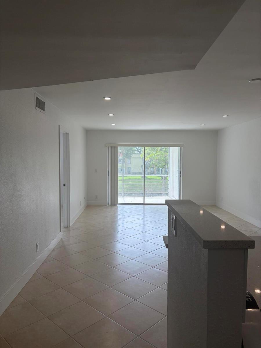 An interior view of a living area with tile flooring, a breakfast bar, and balcony doors — 2900 Fiore Way # 2110, Delray Beach FL 33445, DELRAY BEACH, FL