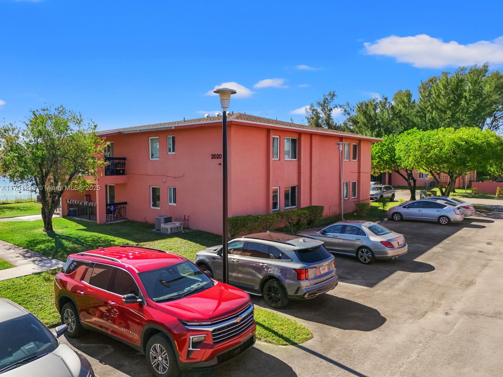 An exterior view of a two-story pink apartment building with a parking lot in front — 2020 NW 119th St # 1122, Miami FL 33167, MIAMI, FL