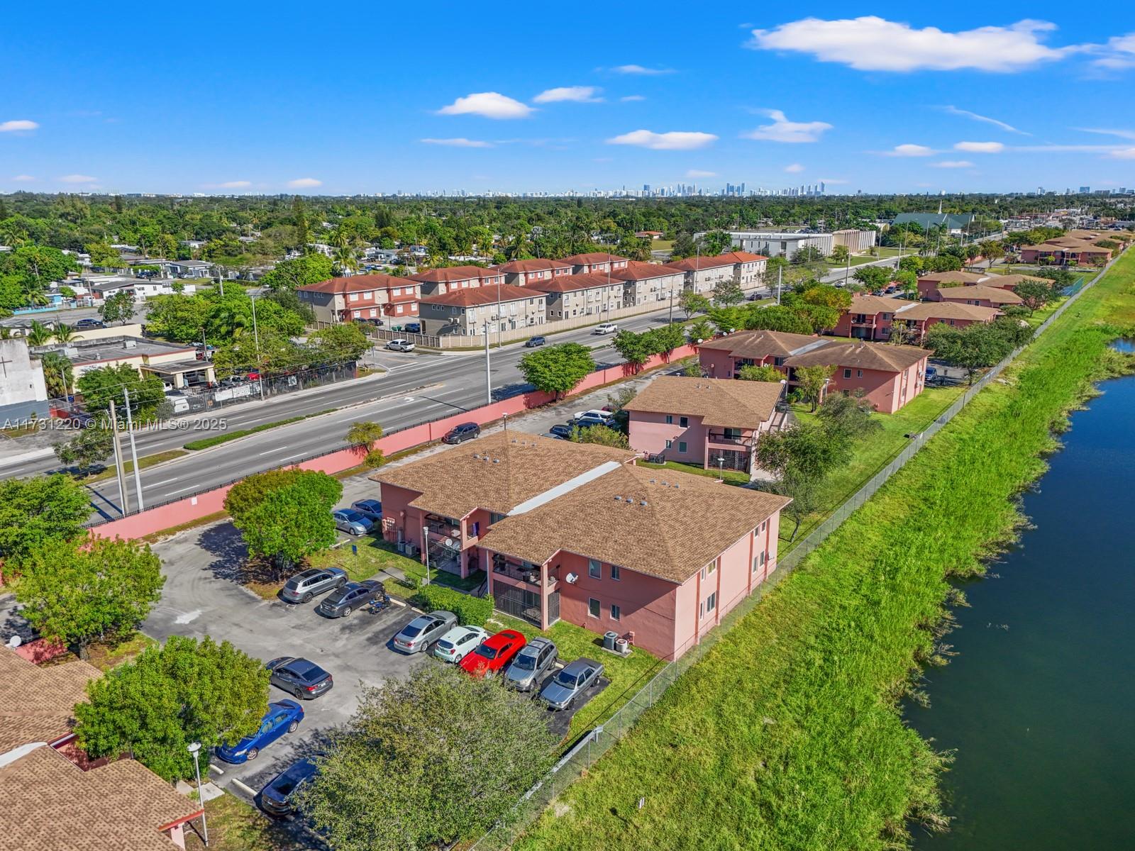 An aerial view shows pink apartment buildings with brown roofs next to a canal — 2020 NW 119th St # 1122, Miami FL 33167, MIAMI, FL
