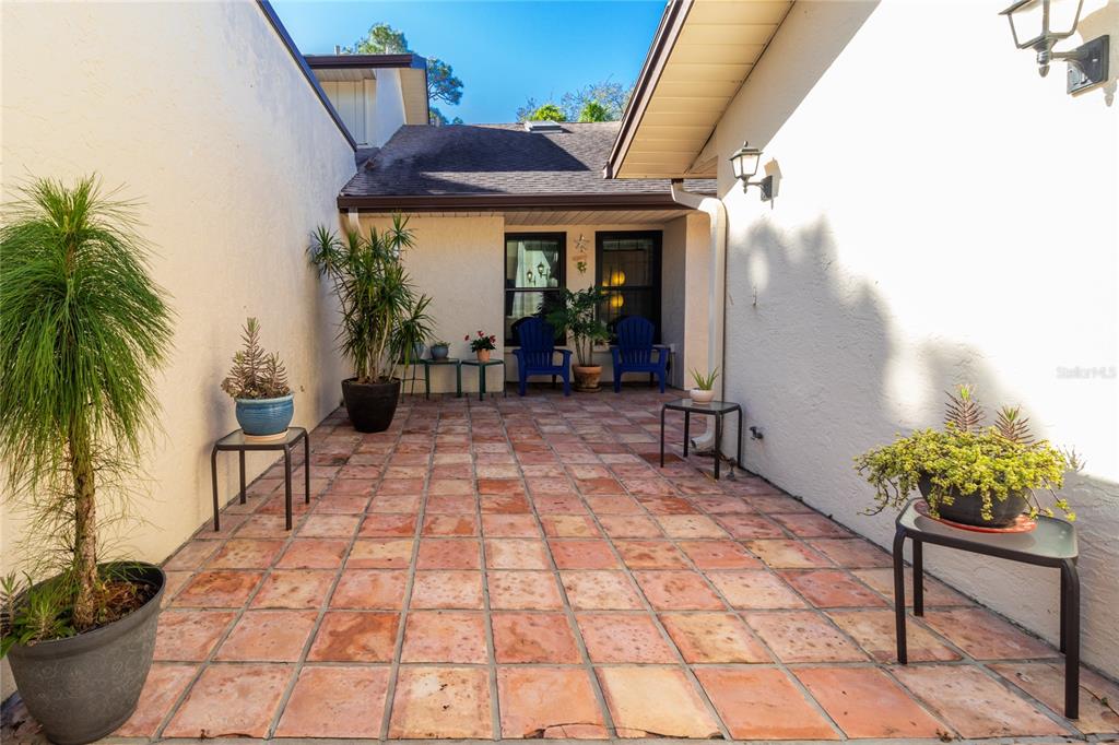 An outdoor courtyard features terracotta tile flooring, potted plants, and two blue chairs — 4660 LA JOLLA DRIVE, BRADENTON, FL