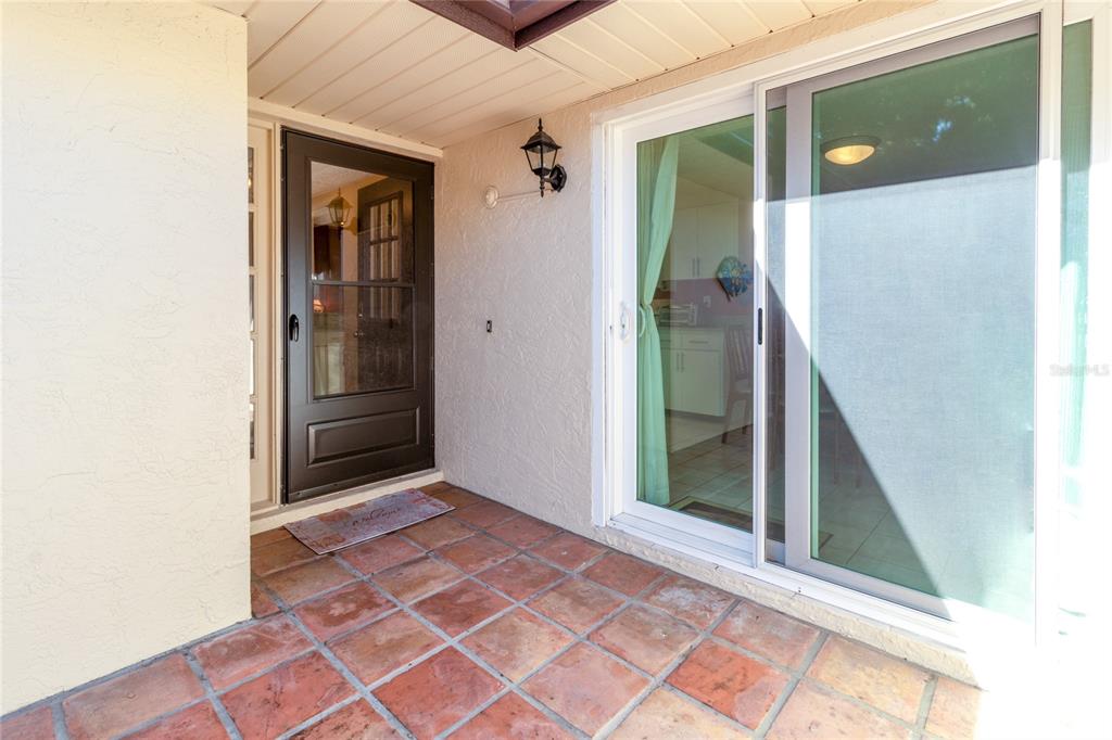 A covered patio features terracotta tile flooring, a dark storm door, and sliding glass doors — 4660 LA JOLLA DRIVE, BRADENTON, FL