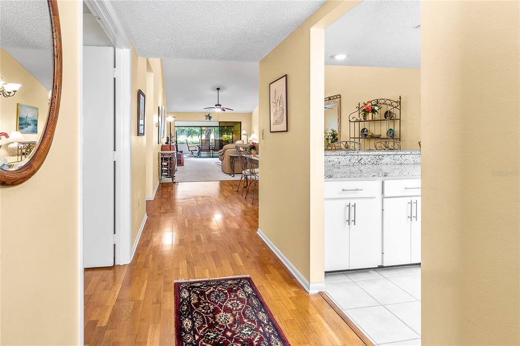 A hallway with hardwood floors leads to a living area with a view of a patio — 4660 LA JOLLA DRIVE, BRADENTON, FL