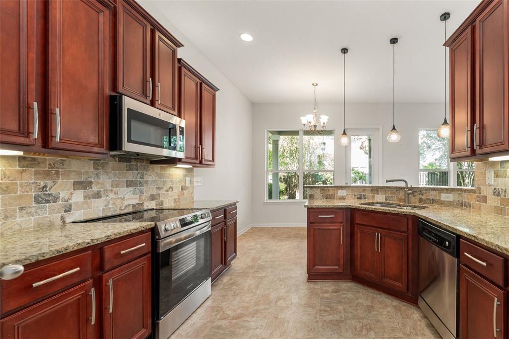 A kitchen with cherry wood cabinets, granite countertops, stainless steel appliances, and a tile backsplash — 8223 NW 53RD STREET, GAINESVILLE, FL