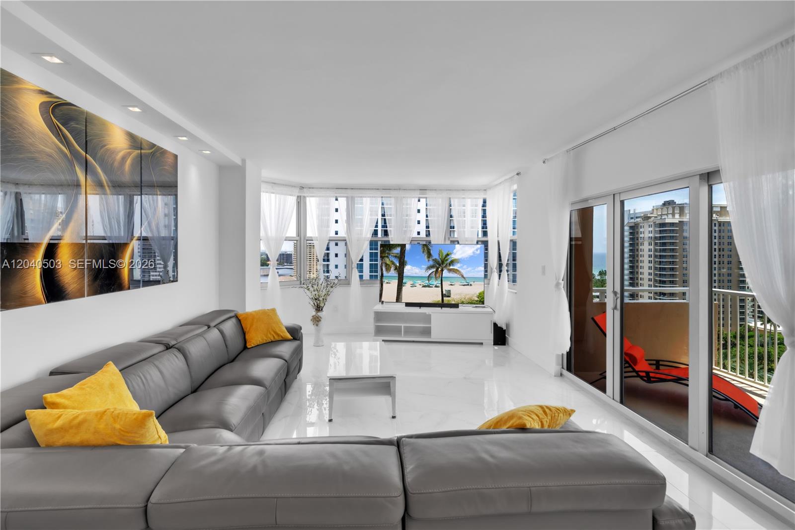 A modern living room features a grey sectional sofa, white tile floors, and balcony views — 1965 S Ocean Dr, Hallandale Beach FL 33009, HALLANDALE BEACH, FL