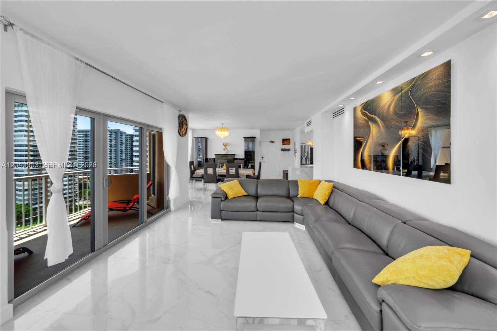 A modern living room features a grey sectional sofa, white marble floors, and a balcony — 1965 S Ocean Dr, Hallandale Beach FL 33009, HALLANDALE BEACH, FL