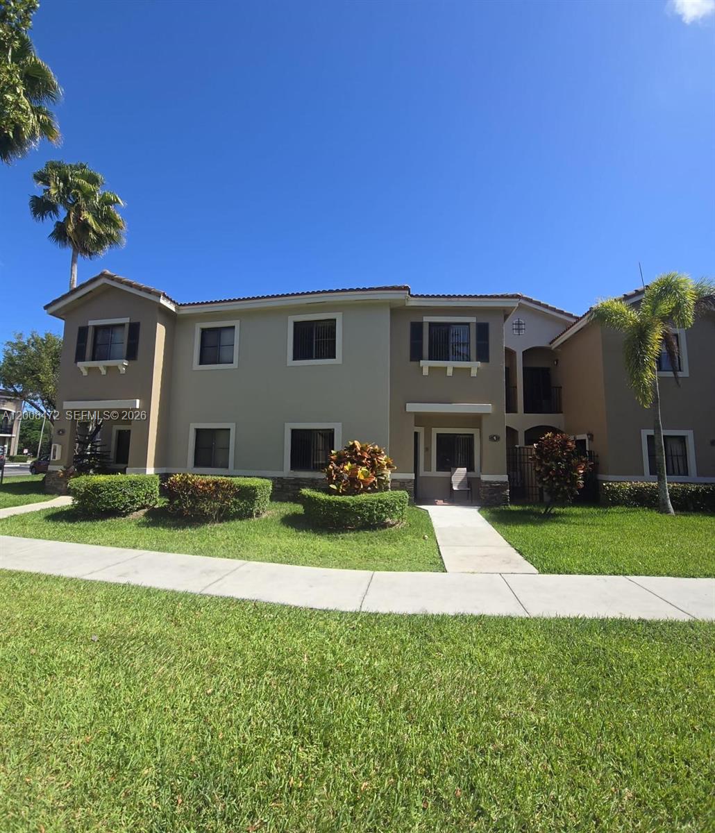 A two-story apartment building with tan stucco walls, dark shutters, and a landscaped front lawn — 22911 SW 88th Pl # 21, Cutler Bay FL 33190, CUTLER BAY, FL