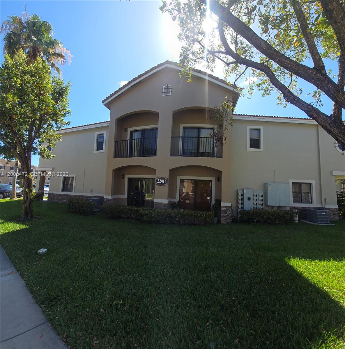 A two-story residential building features a tan stucco exterior with balconies and a lawn — 22911 SW 88th Pl # 21, Cutler Bay FL 33190, CUTLER BAY, FL