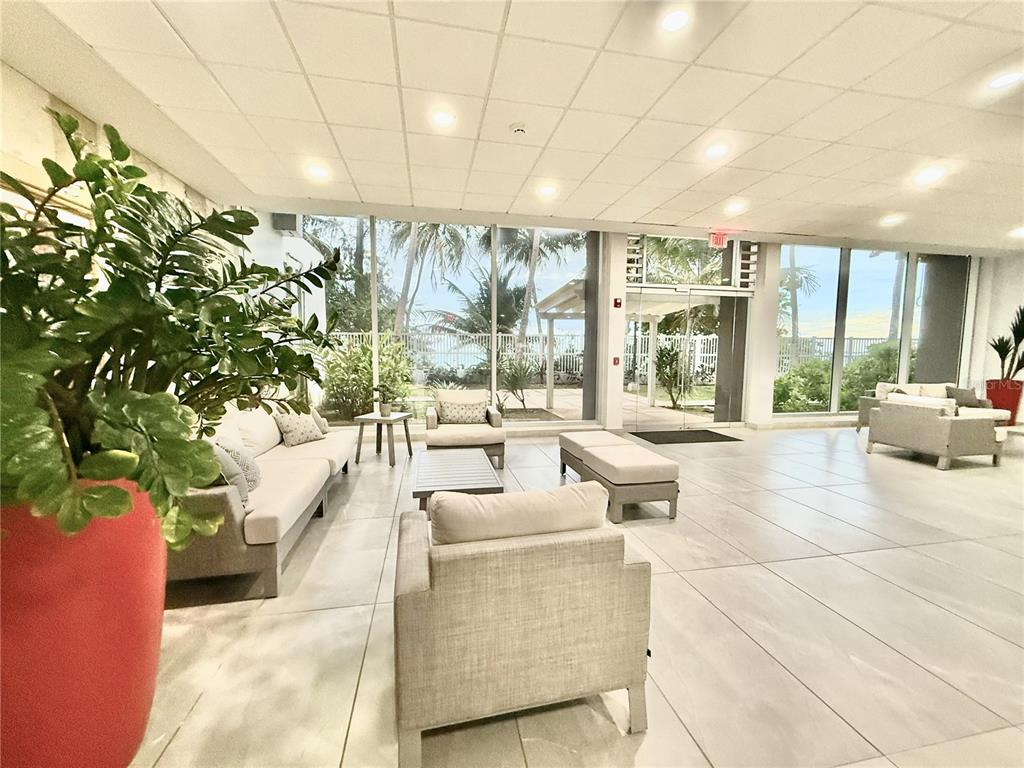 A bright lobby features tile flooring, modern seating, and floor-to-ceiling windows overlooking a patio — 3103 AV. ISLA VERDE UNIT 306, CAROLINA, PR