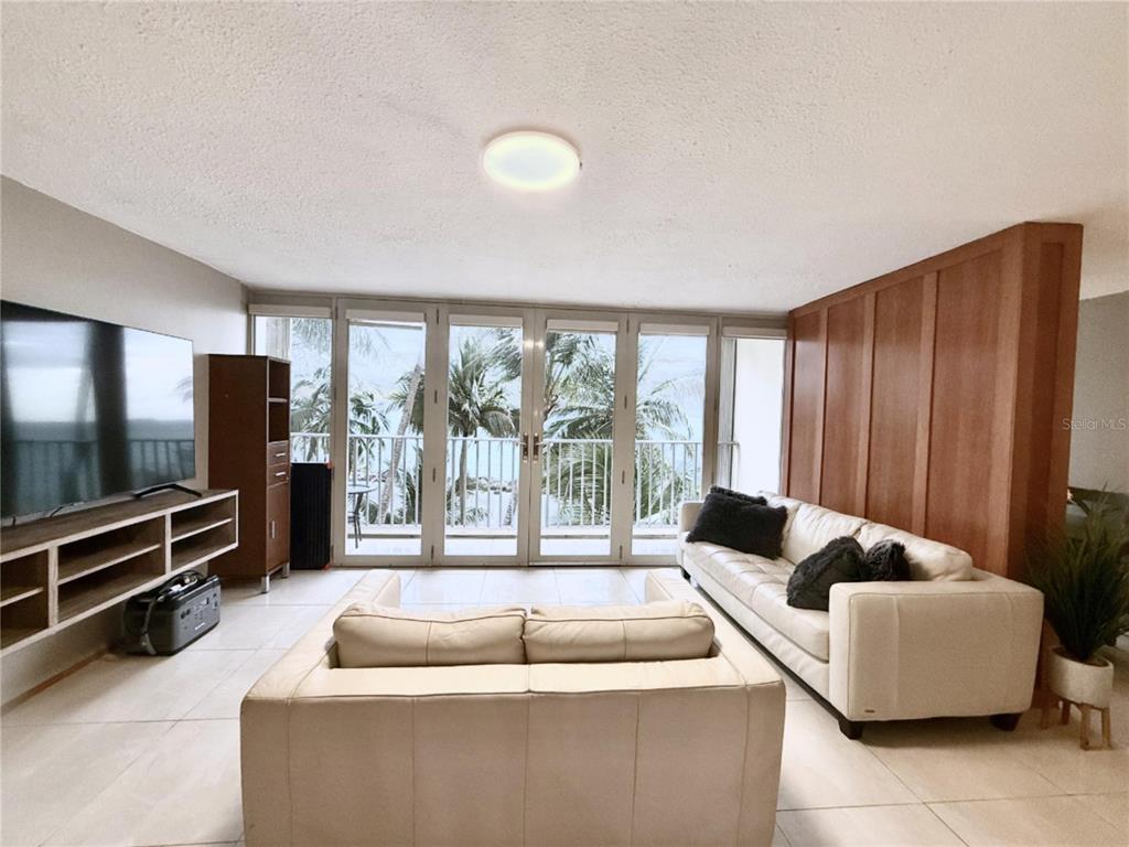 A living room features white tile floors, a white sofa, and glass doors overlooking palm trees — 3103 AV. ISLA VERDE UNIT 306, CAROLINA, PR