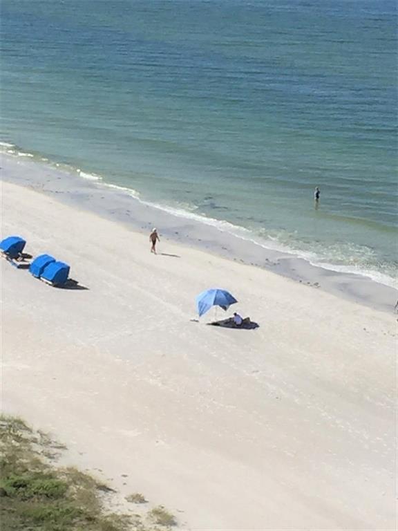 An elevated view of a sandy beach with blue umbrellas and people near the water — 17408 GULF BOULEVARD UNIT 1003, REDINGTON SHORES, FL