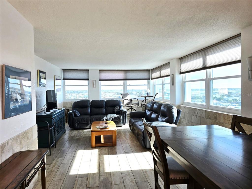 A living and dining area features tile floors, leather sofas, and large windows with water views — 17408 GULF BOULEVARD UNIT 1003, REDINGTON SHORES, FL