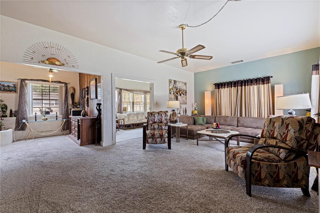 A carpeted living room features a sectional sofa, patterned armchairs, and a ceiling fan — 726 17TH AVENUE S, ST PETERSBURG, FL