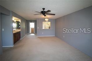 A living room with beige carpet, a ceiling fan, and a pass-through to the kitchen — 255 MISSION TRAIL S UNIT J, VENICE, FL
