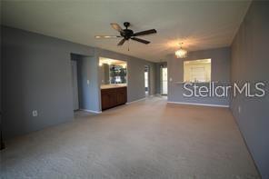 A spacious living area features beige carpeting, gray walls, a ceiling fan, and an open kitchen — 255 MISSION TRAIL S UNIT J, VENICE, FL