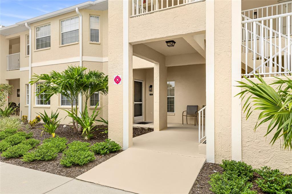 An exterior view of a beige apartment building with a covered entryway and palm trees — 5800 SABAL TRACE DRIVE UNIT 105, NORTH PORT, FL