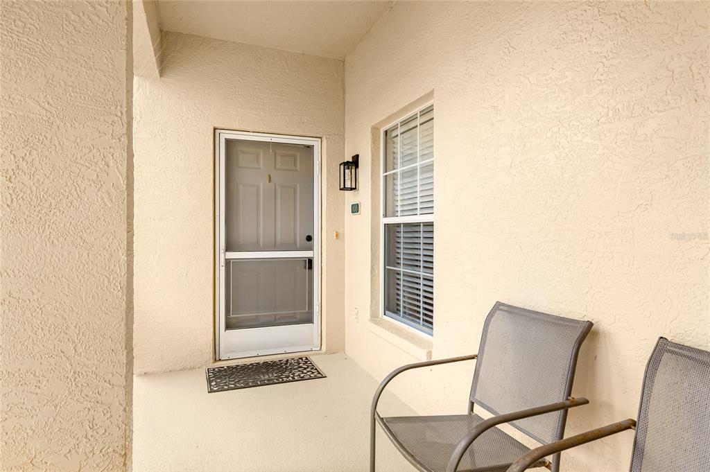 A covered entryway features a beige stucco wall, a screen door, and two outdoor chairs — 5800 SABAL TRACE DRIVE UNIT 105, NORTH PORT, FL