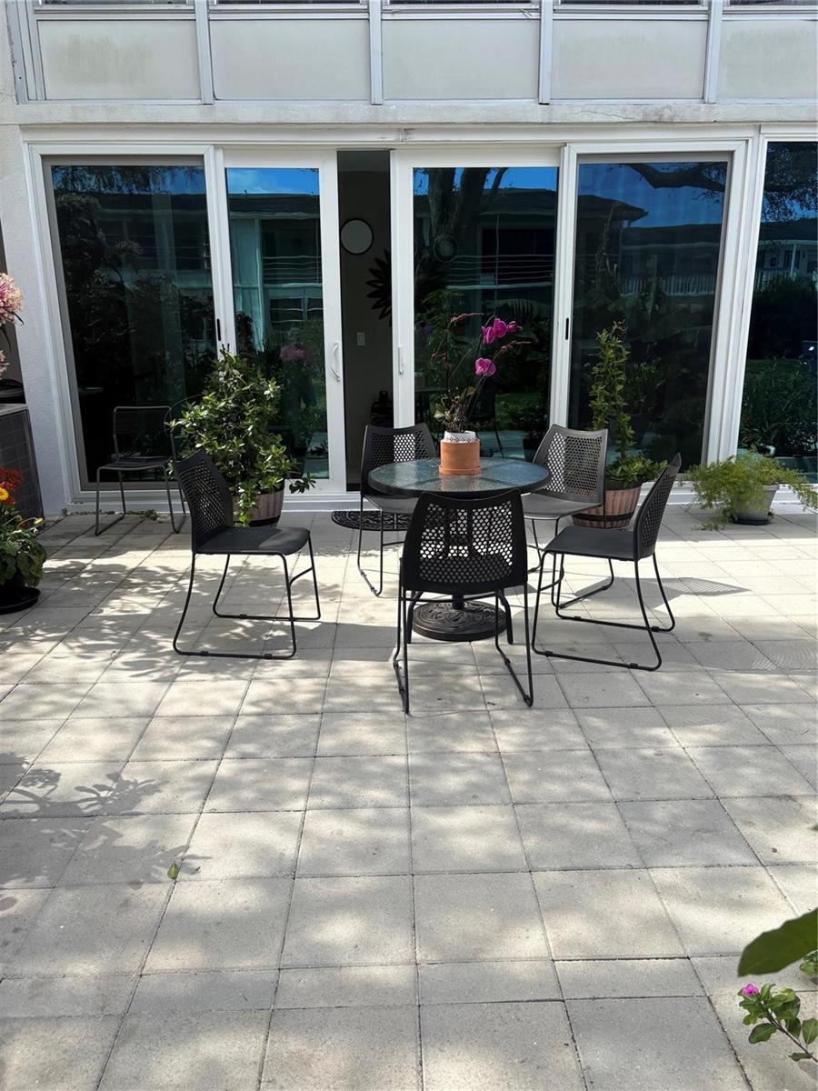 A patio features a small round glass table with four black chairs and potted plants — 211 N Oakridge # 211, Deerfield Beach FL 33442, DEERFIELD BEACH, FL