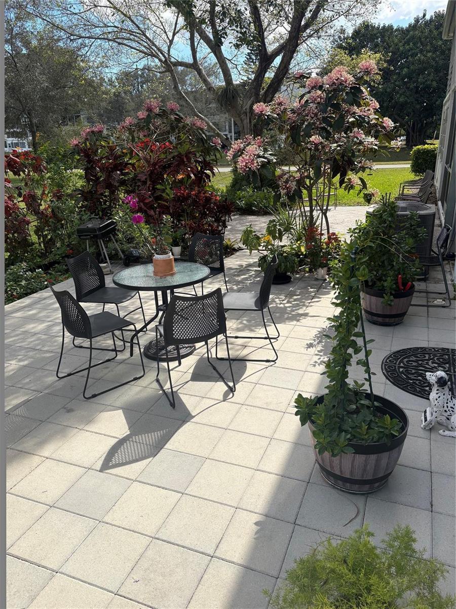 A paved patio features a round glass table with four chairs and various potted plants — 211 N Oakridge # 211, Deerfield Beach FL 33442, DEERFIELD BEACH, FL