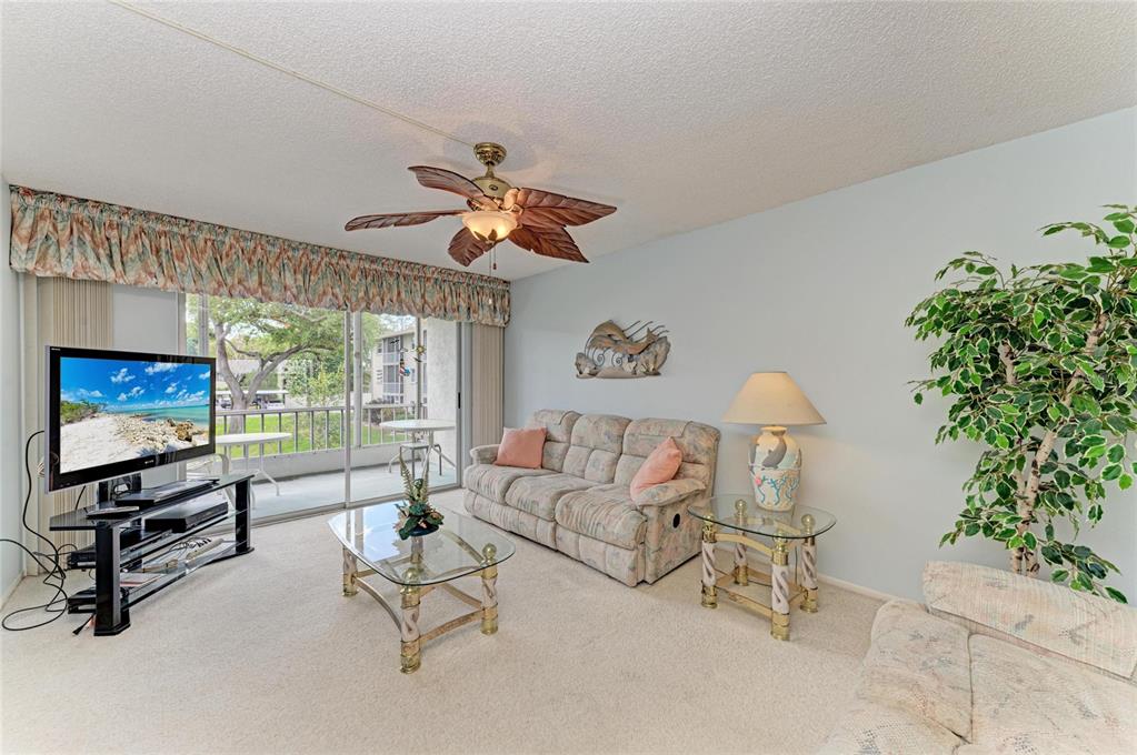 A living room features a floral sofa, glass-topped tables, a ceiling fan, and sliding doors — 3983 MACEACHEN BOULEVARD UNIT 424, SARASOTA, FL
