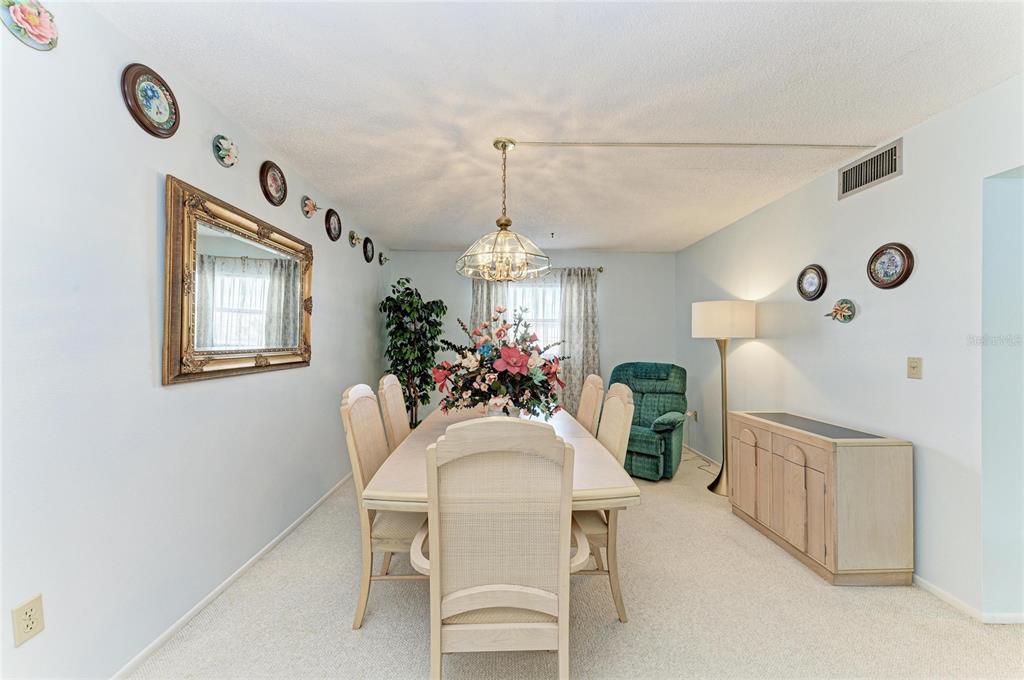 A dining room features a light-colored table with six chairs, a chandelier, and wall decor — 3983 MACEACHEN BOULEVARD UNIT 424, SARASOTA, FL