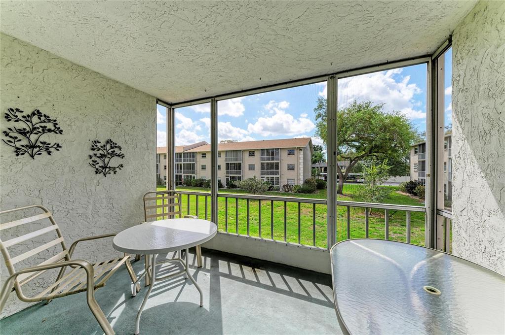 A screened-in balcony features a small table, chairs, and a view of a neighboring building — 3983 MACEACHEN BOULEVARD UNIT 424, SARASOTA, FL