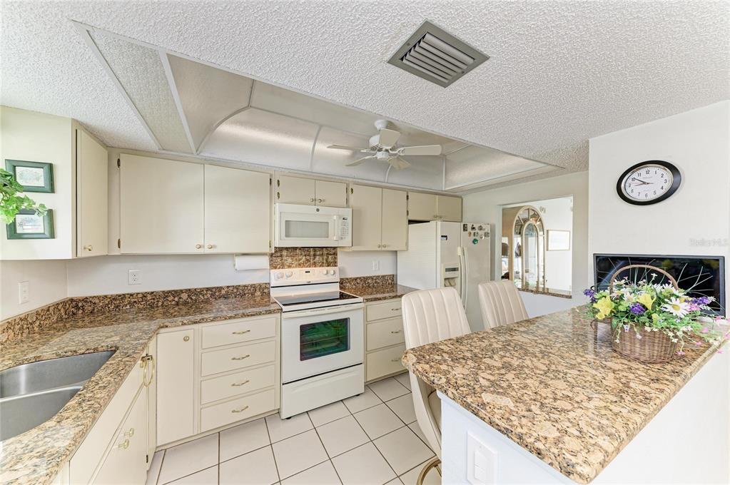 A kitchen features cream cabinets, granite countertops, a white stove, and a breakfast bar — 3983 MACEACHEN BOULEVARD UNIT 424, SARASOTA, FL