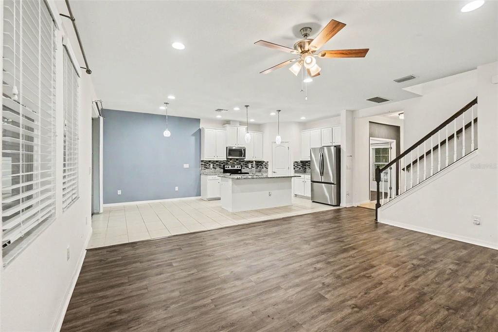 An open-concept living room with wood-look flooring leads to a kitchen with white cabinets — 12112 LEDBURY COMMONS DRIVE, GIBSONTON, FL