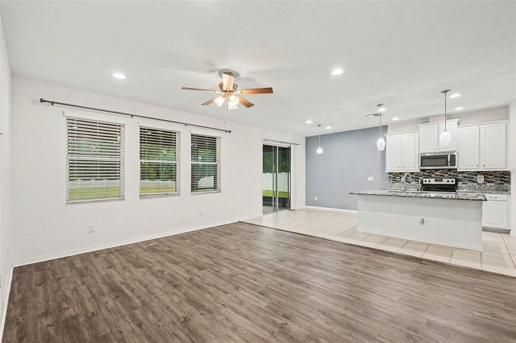 An open-concept living room with wood-look flooring transitions into a tiled kitchen area — 12112 LEDBURY COMMONS DRIVE, GIBSONTON, FL