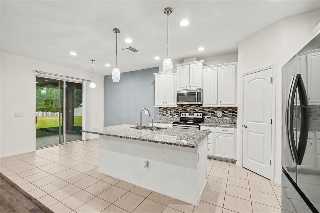 A kitchen features white cabinets, granite countertops, a center island, and a sliding glass door — 12112 LEDBURY COMMONS DRIVE, GIBSONTON, FL