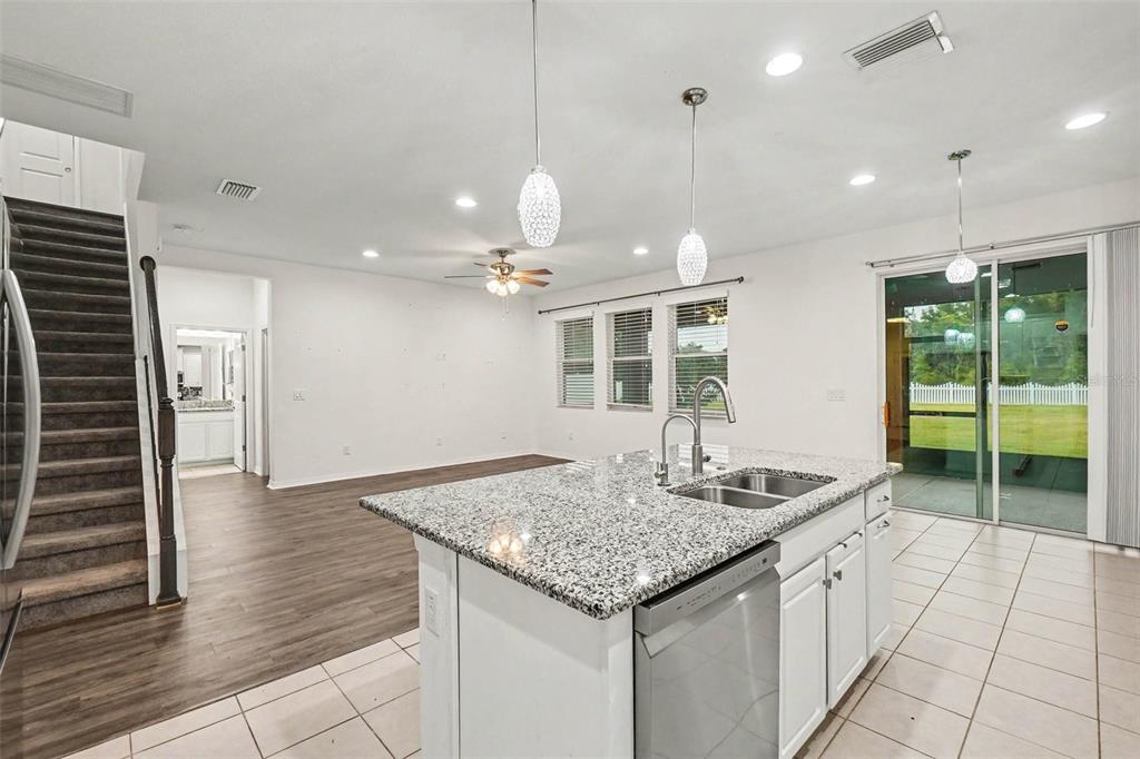 A kitchen island with granite countertops sits in front of a living area and staircase — 12112 LEDBURY COMMONS DRIVE, GIBSONTON, FL