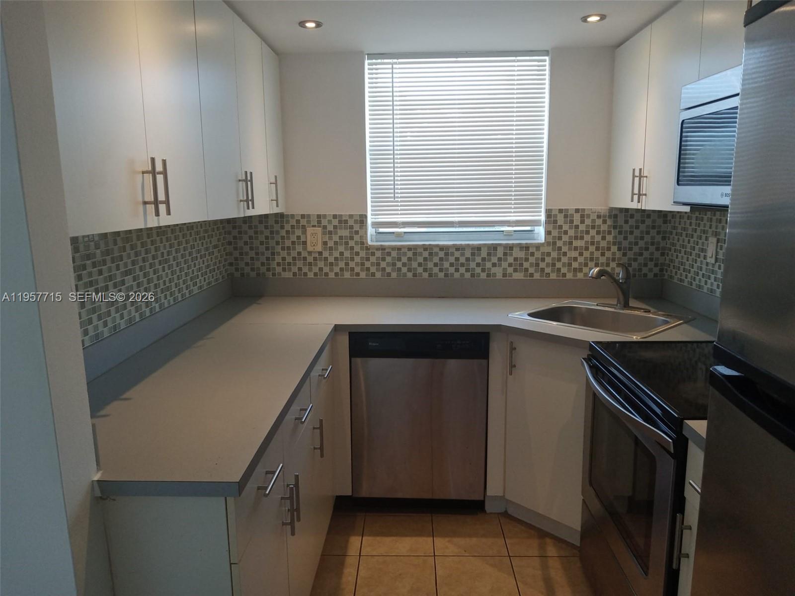 A galley kitchen features white cabinets, stainless steel appliances, gray countertops, and a tiled backsplash — 1975 NE 135th St # 3C, North Miami FL 33181, NORTH MIAMI, FL