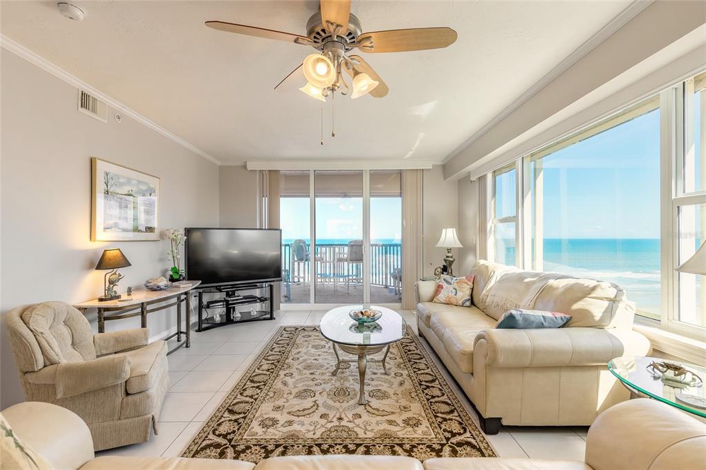 A living room with a beige sofa, patterned rug, ceiling fan, and ocean view windows — 4631 S ATLANTIC AVENUE UNIT 8607, PORT ORANGE, FL