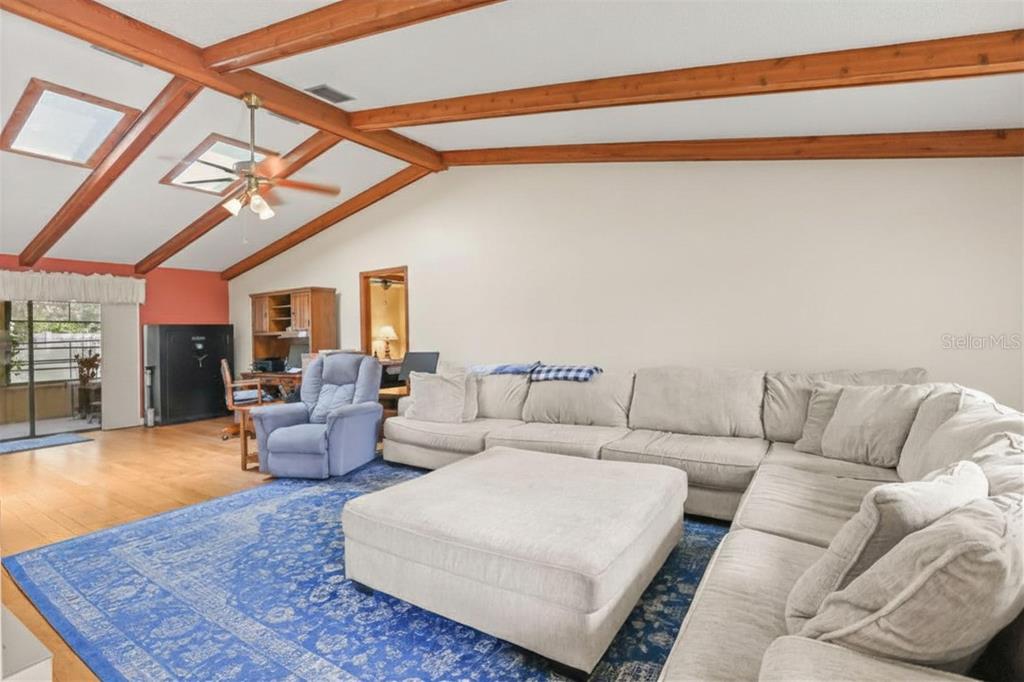 A living room features a vaulted ceiling with exposed wood beams, a large sectional, and rug — 1573 SKYE COURT, APOPKA, FL