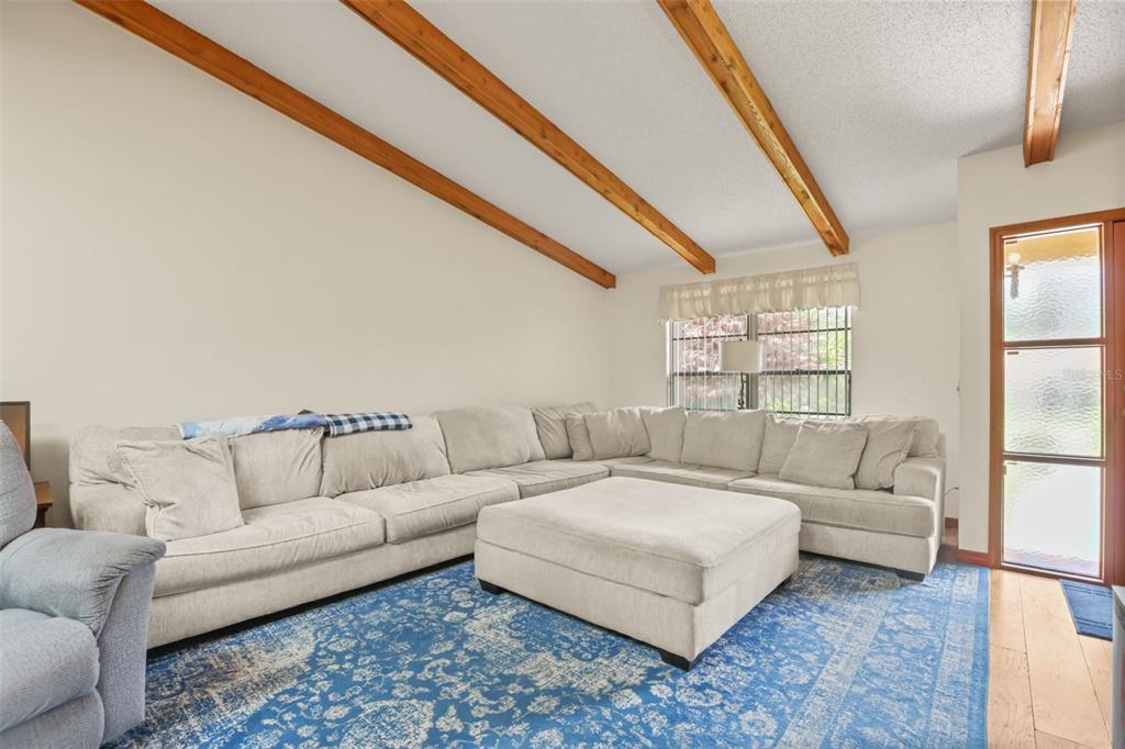A living room features a large sectional sofa, a blue area rug, and exposed ceiling beams — 1573 SKYE COURT, APOPKA, FL
