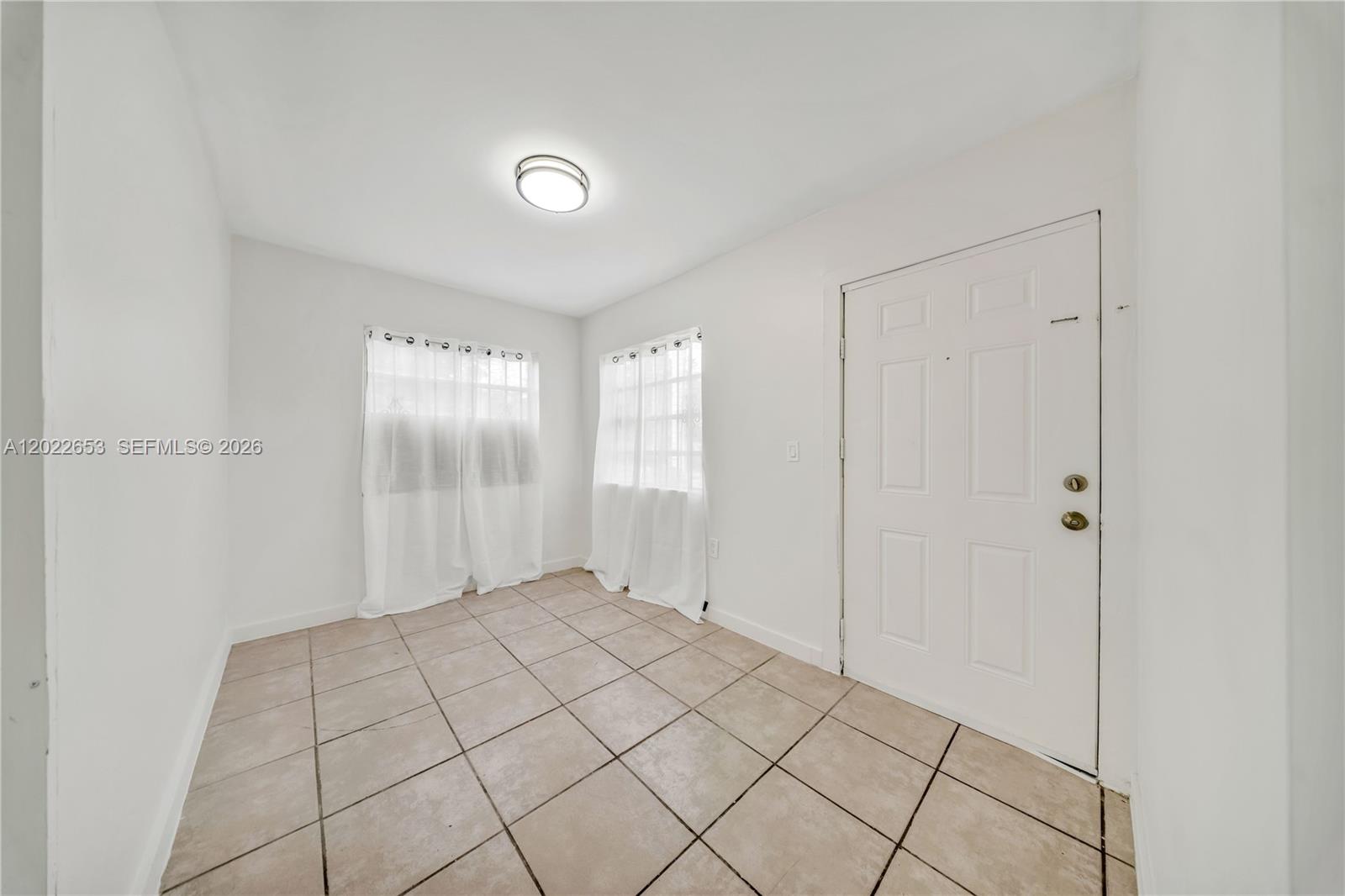 A small room with white walls, tiled flooring, two windows with curtains, and a door — 2744 SW 16th Ter, Miami FL 33145, MIAMI, FL