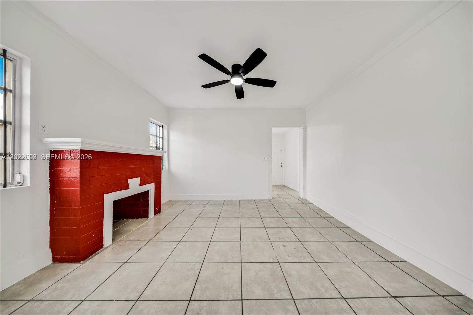 An empty room features white walls, light tile flooring, a ceiling fan, and a red fireplace — 2744 SW 16th Ter, Miami FL 33145, MIAMI, FL