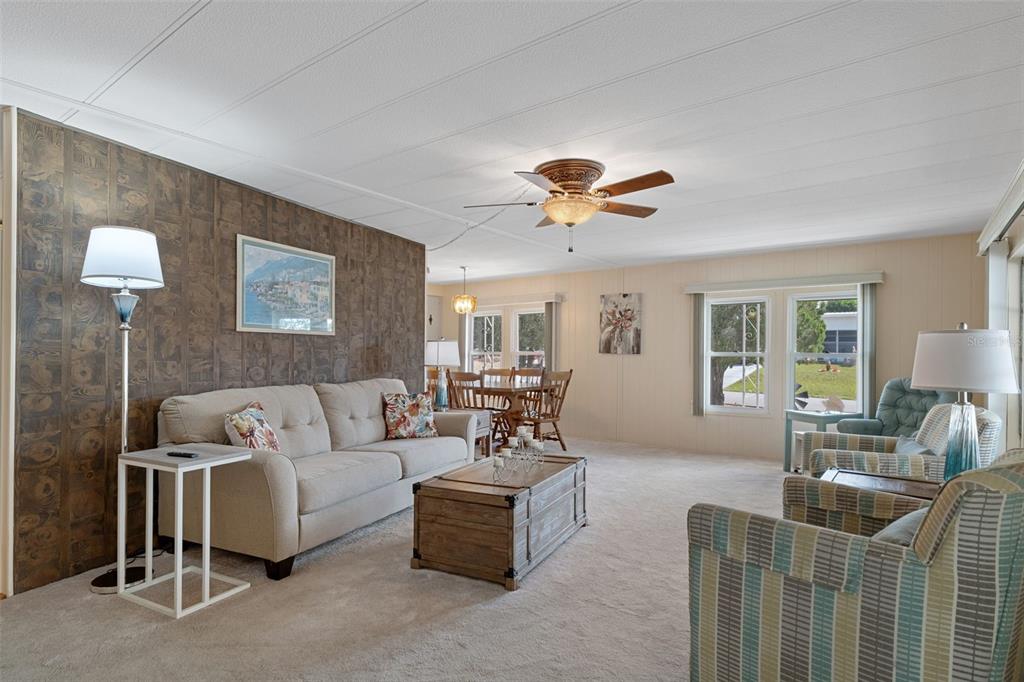 A living room with a wood-paneled accent wall, beige carpet, and a dining area beyond — 8199 MODENA AVENUE, BROOKSVILLE, FL