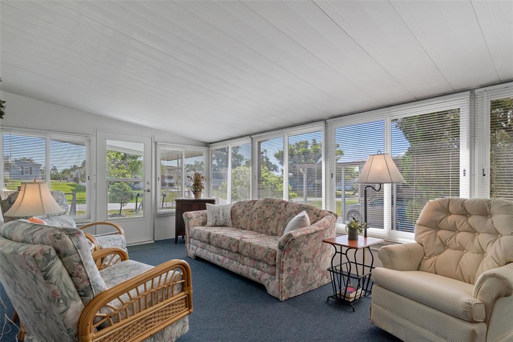 A sunroom with blue carpeting, a floral sofa, two armchairs, and large windows with blinds — 8199 MODENA AVENUE, BROOKSVILLE, FL
