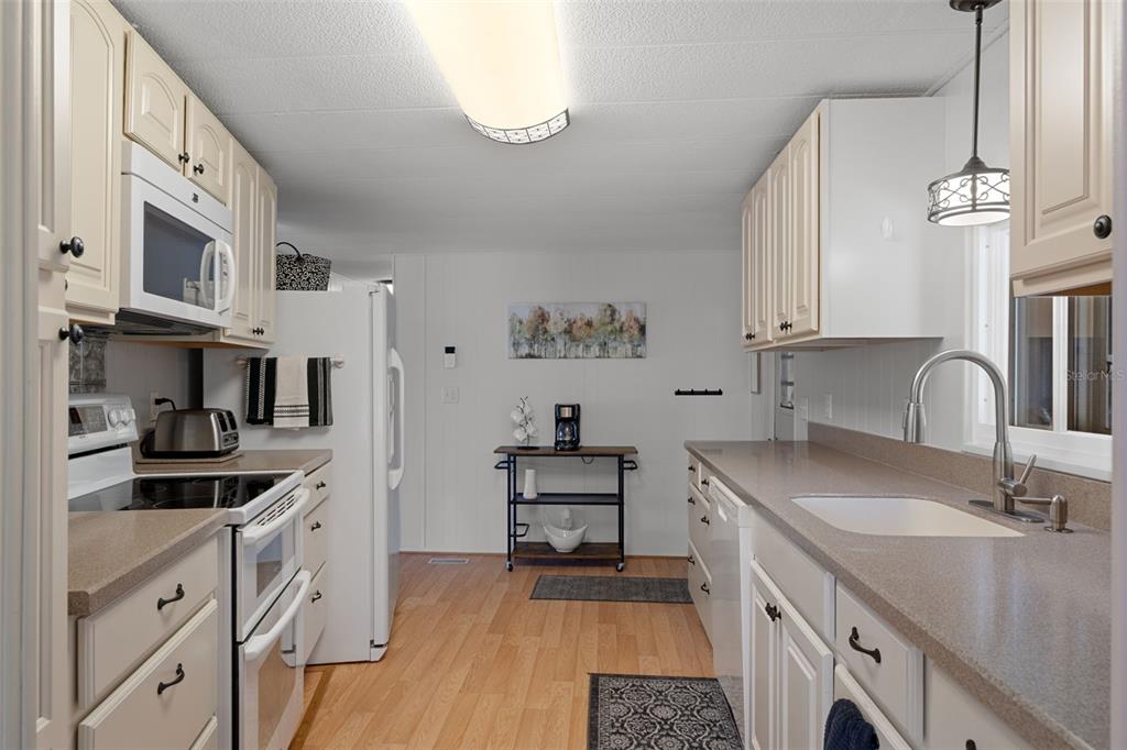 A galley kitchen features white cabinets, light countertops, stainless steel appliances, and wood-look flooring — 8199 MODENA AVENUE, BROOKSVILLE, FL