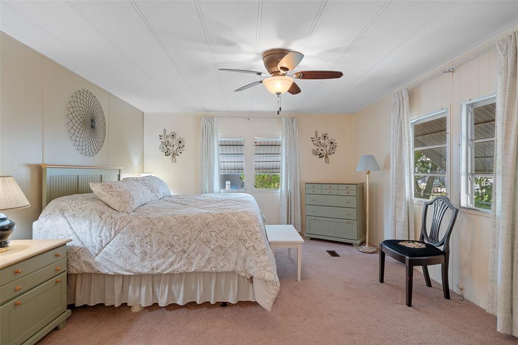 A bedroom features a bed, green dressers, a ceiling fan, and windows with white curtains — 8199 MODENA AVENUE, BROOKSVILLE, FL