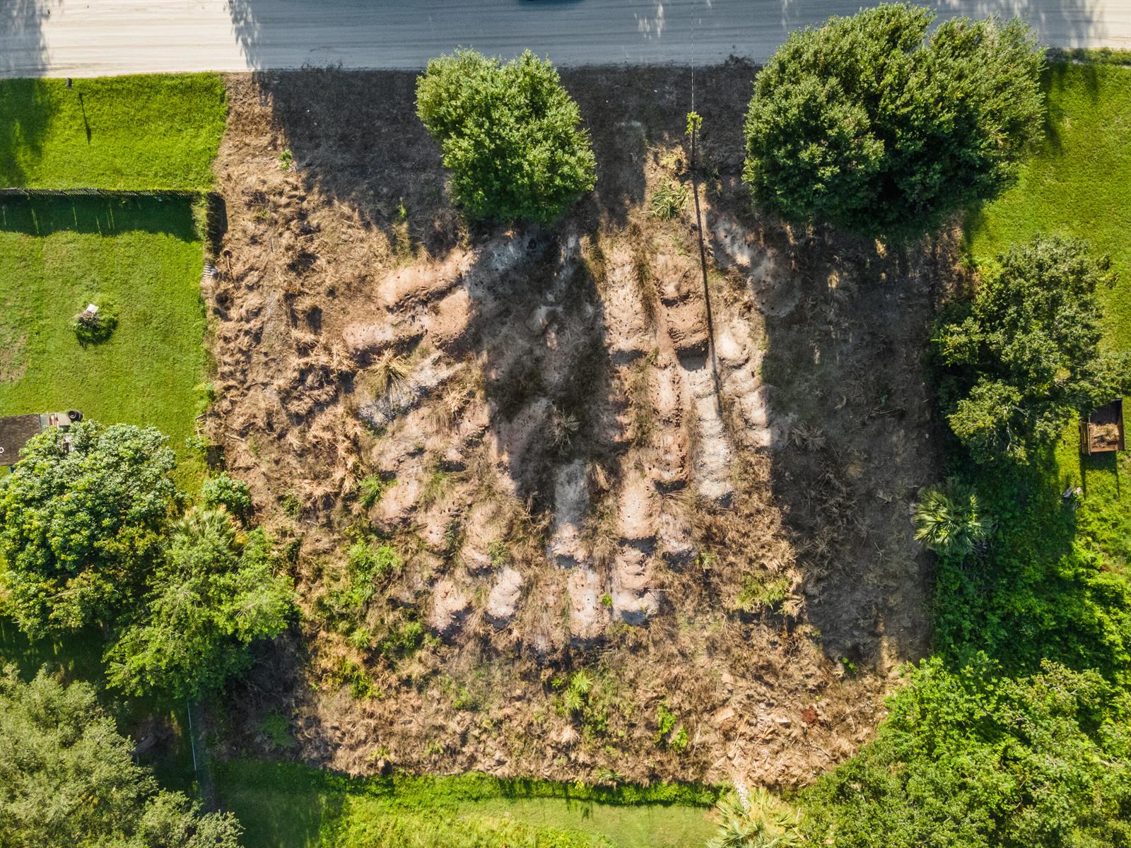 An aerial view shows a cleared, uneven dirt lot surrounded by trees and residential lawns — 8720 92nd Avenue, Vero Beach FL 32967, VERO BEACH, FL