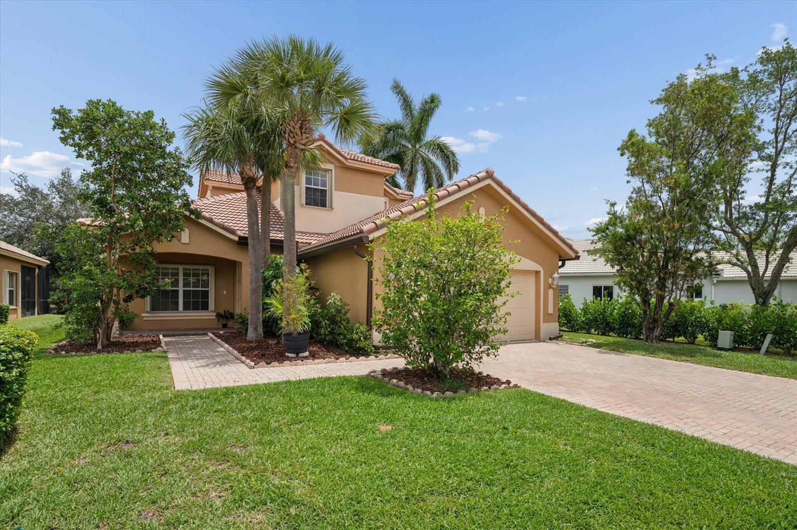 A two-story tan stucco house with a tiled roof, palm trees, and a paved driveway — 11259 NW 65th Manor, Parkland FL 33076, PARKLAND, FL