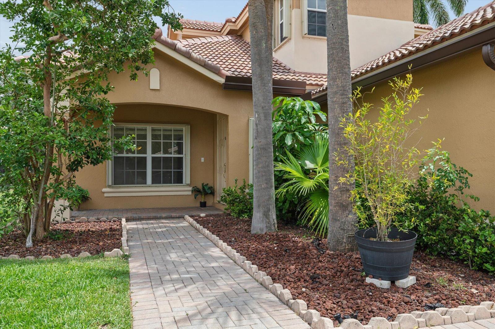 A paved walkway leads to the front entrance of a tan stucco home with landscaping — 11259 NW 65th Manor, Parkland FL 33076, PARKLAND, FL