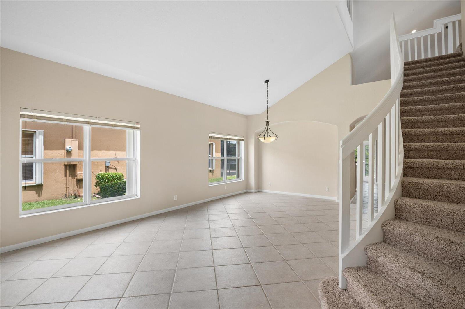 A bright, empty living room with tiled floors, a vaulted ceiling, and a carpeted staircase — 11259 NW 65th Manor, Parkland FL 33076, PARKLAND, FL
