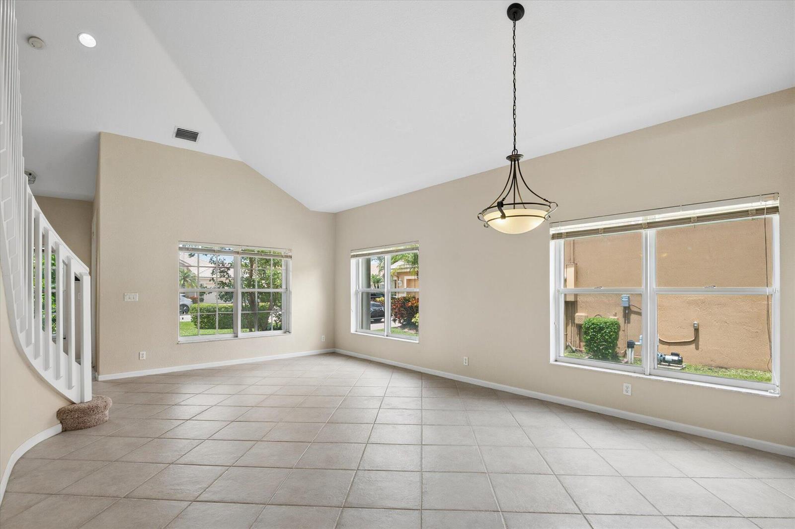 An empty living room with vaulted ceilings, tile floors, a chandelier, and three windows — 11259 NW 65th Manor, Parkland FL 33076, PARKLAND, FL