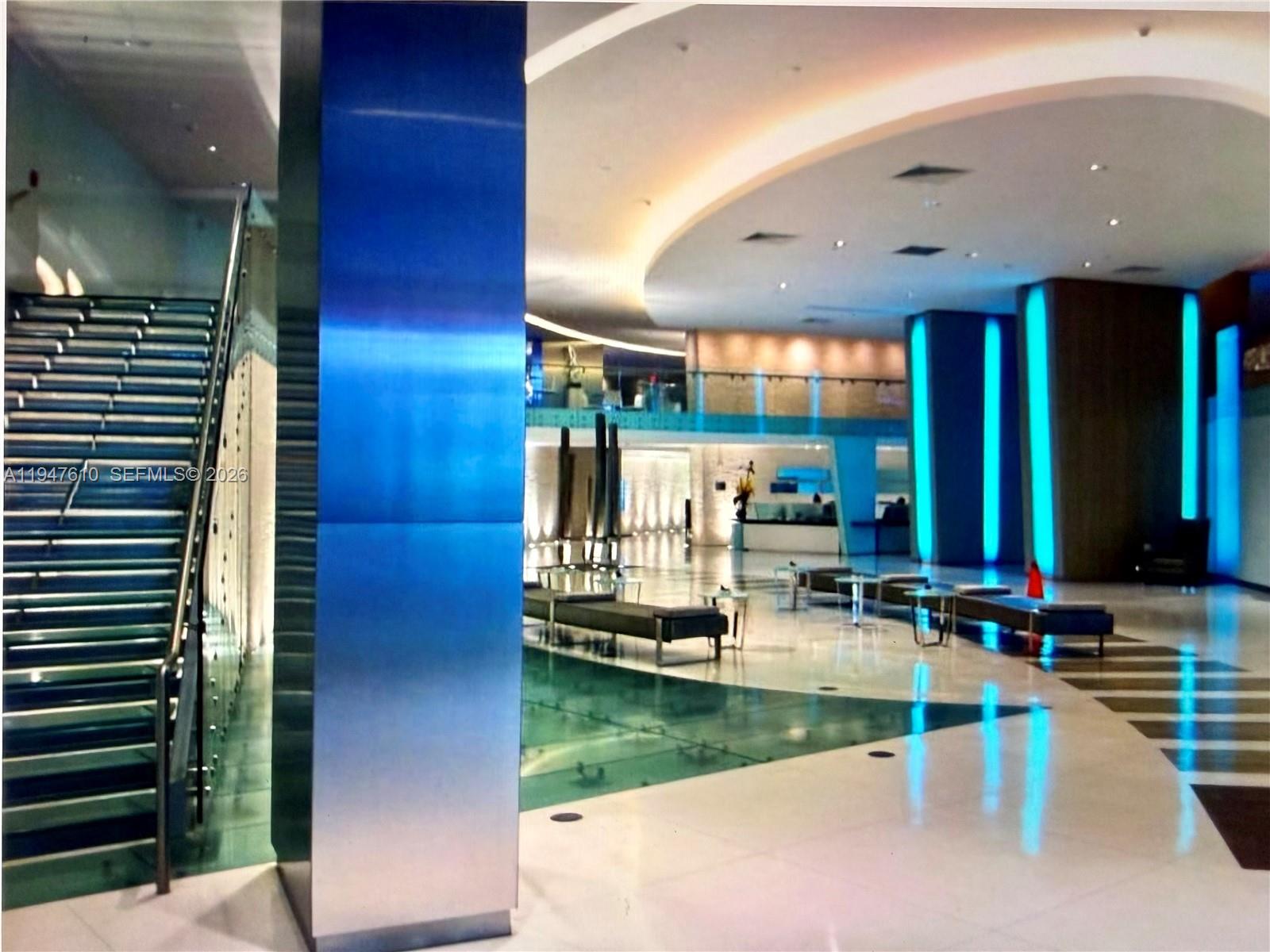 A modern building lobby features a glass staircase, polished floors, and blue-lit structural columns — 92 SW 3rd St # 4709, Miami FL 33130, MIAMI, FL