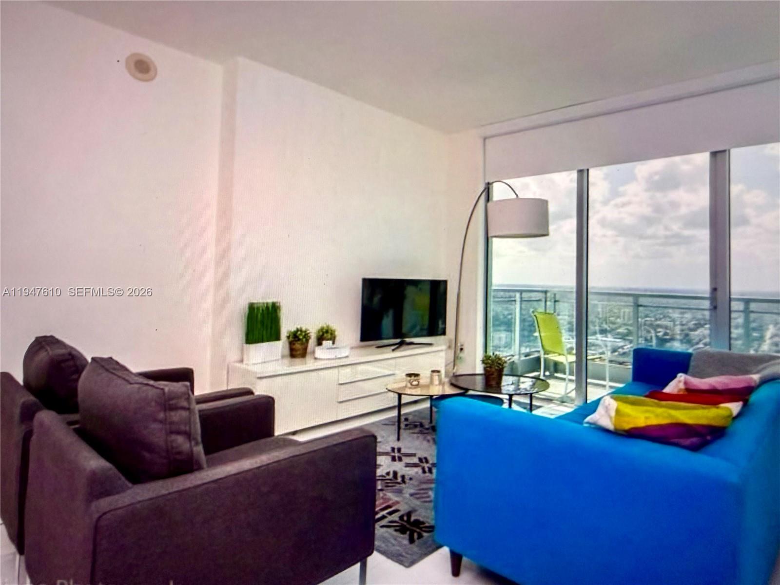 A living room features a blue sofa, dark armchairs, a television, and a balcony view — 92 SW 3rd St # 4709, Miami FL 33130, MIAMI, FL